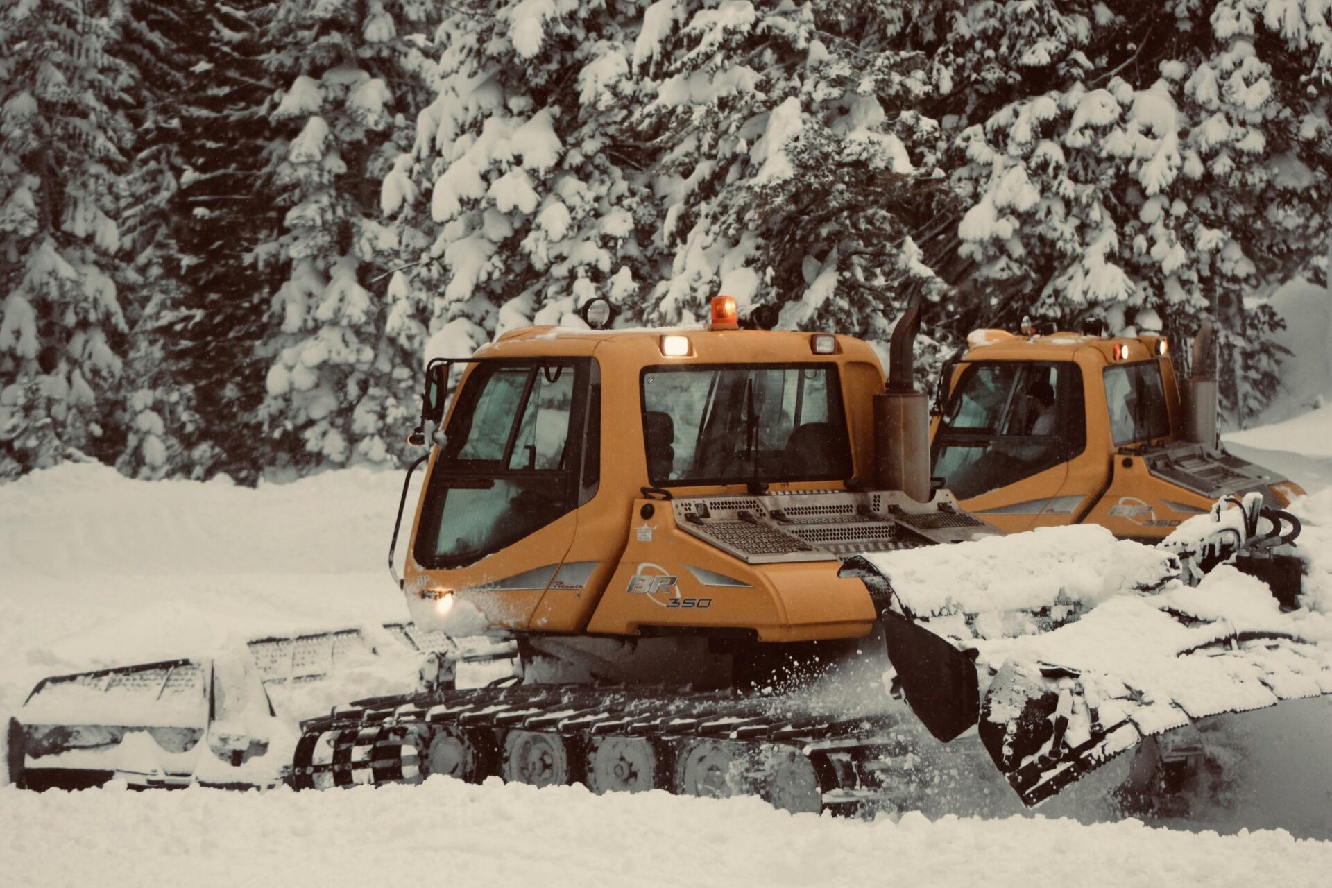 Snow cat working an orange-lit storm shift in the high country