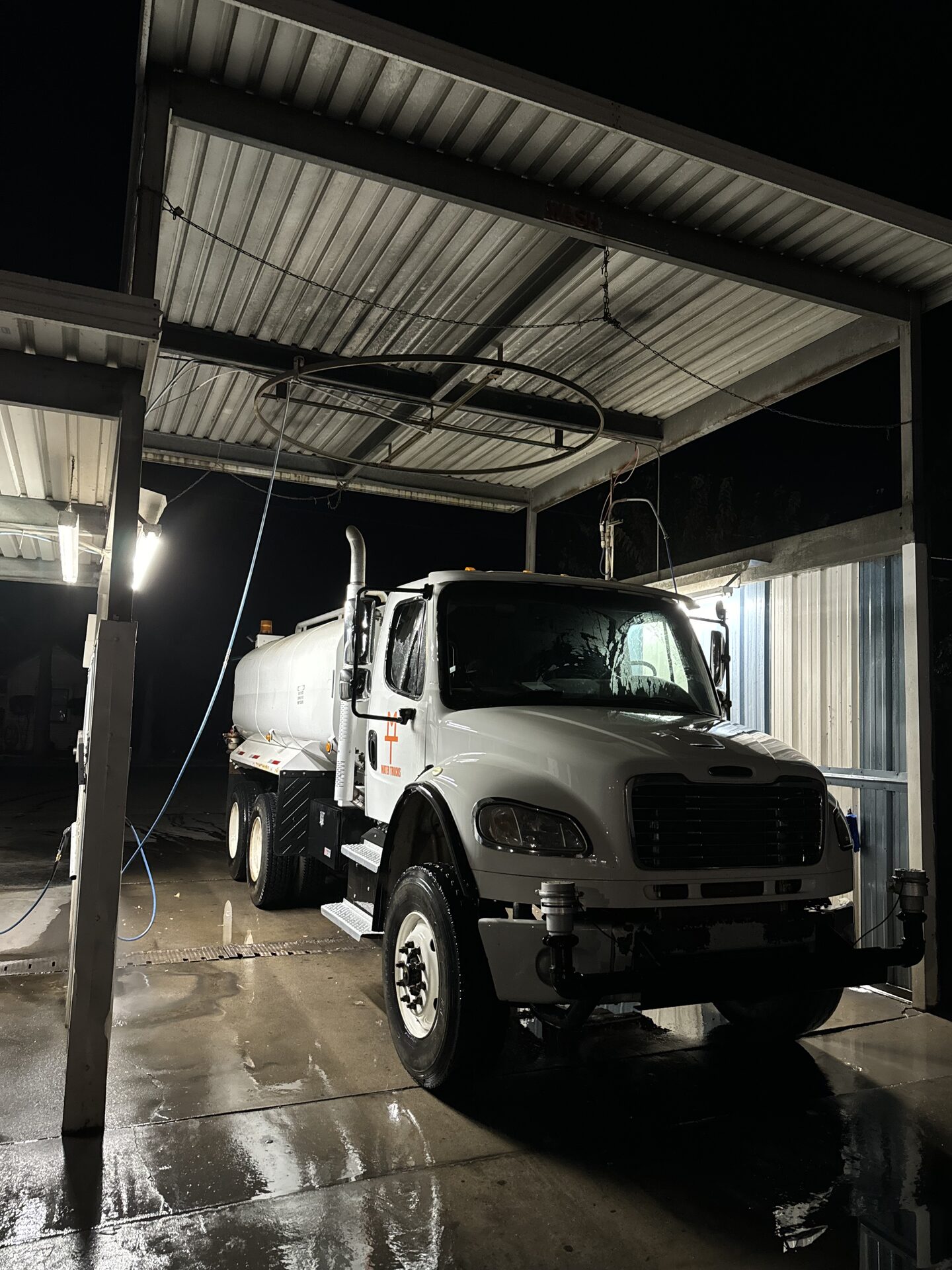 CKJ Ag Services Freightliner water truck in the wash bay at night